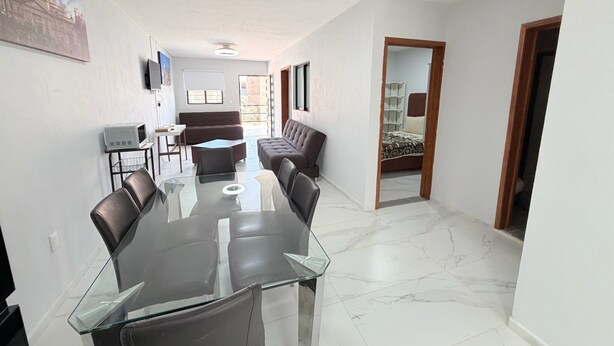 A modern living room with a glass dining table, leather sofas, a TV, and a large window. - Residencia Gran Coyula Orange 510A (Tonala)