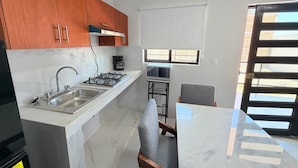 A compact kitchen with a gas stove, sink, and a microwave. - Residencia Gran Coyula Orange 508A (Tonala)