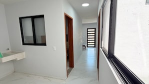 A hallway with a white tiled floor, a window with a black frame, and a door leading to another room. - Residencia Gran Coyula Orange 508A (Tonala)
