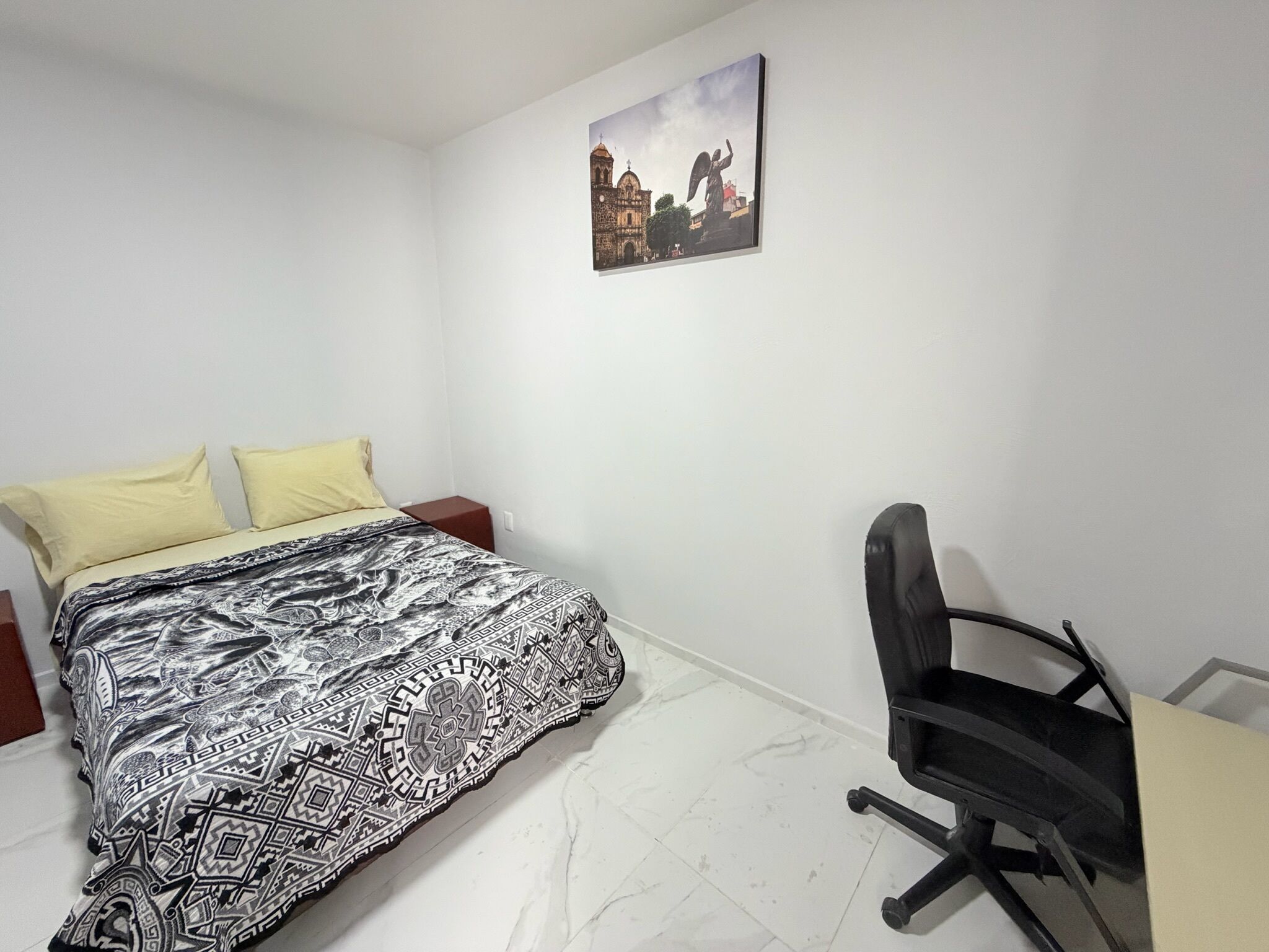 A bedroom with a bed, two pillows, a desk, and a chair.