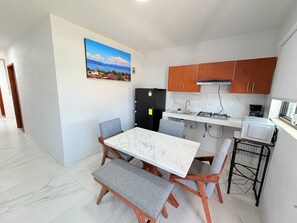 Une cuisine compacte dotée d’un plan de travail en marbre, de meubles en bois, d’un réfrigérateur noir, d’une cuisinière à gaz et d’un four à micro-ondes.