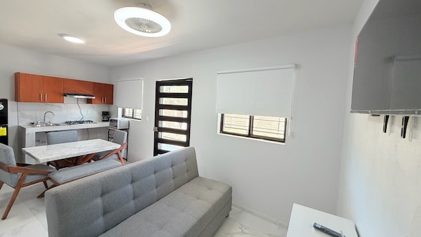 A modern kitchen with a gas stove, a microwave, and a sink. There is a dining table with chairs and a grey sofa. - Residencia Gran Coyula Orange 508A (Tonala)