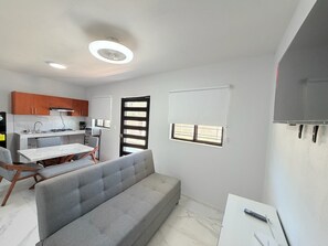 Eine moderne Küche mit Gasherd, Mikrowelle und Spüle. Ein Esstisch mit Stühlen und ein graues Sofa sind ebenfalls vorhanden.