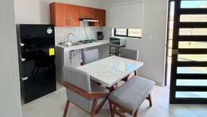 A compact kitchen with modern appliances, a dining table with four chairs, and a view through a sliding door. - Residencia Gran Coyula Orange 508A (Tonala)