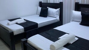 Et hotelværelse med to senge, hvide sengetøj, sorte sengegavl og et flisegulv.