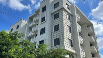 Un edificio de varios pisos con balcones, cielo despejado y algunos árboles en primer plano.