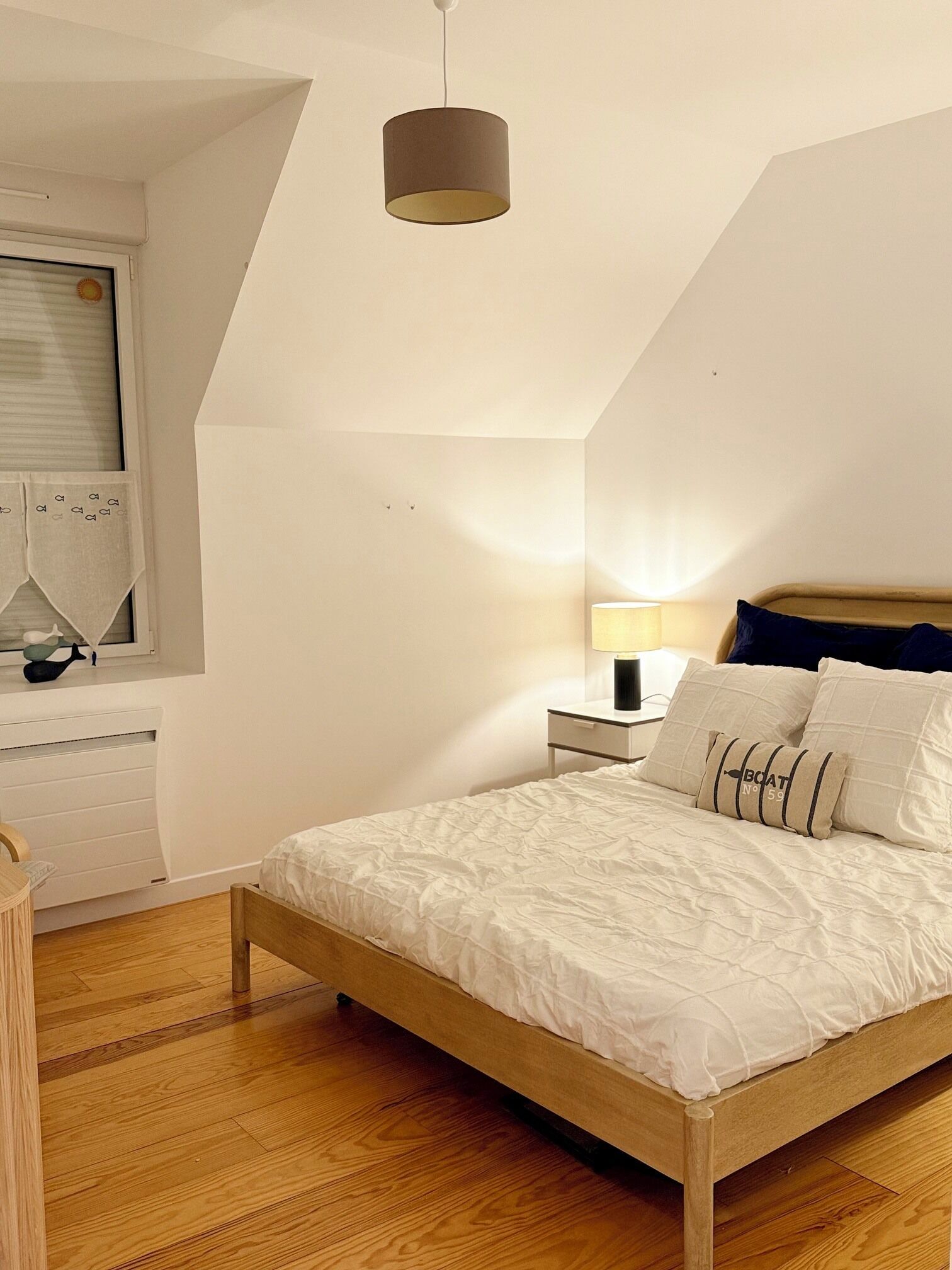 Una camera da letto con un letto in legno, un comodino con una lampada, una finestra con persiane e una plafoniera.