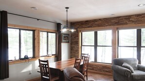 Zona pranzo con tavolo in legno, sedie e una poltrona grigia.