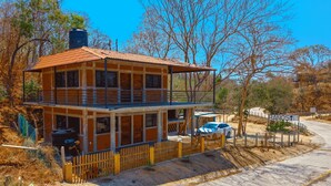 A two-story building with a balcony, a fenced yard, and a parked car. - Casa Mariposa (Santa Maria Huatulco)