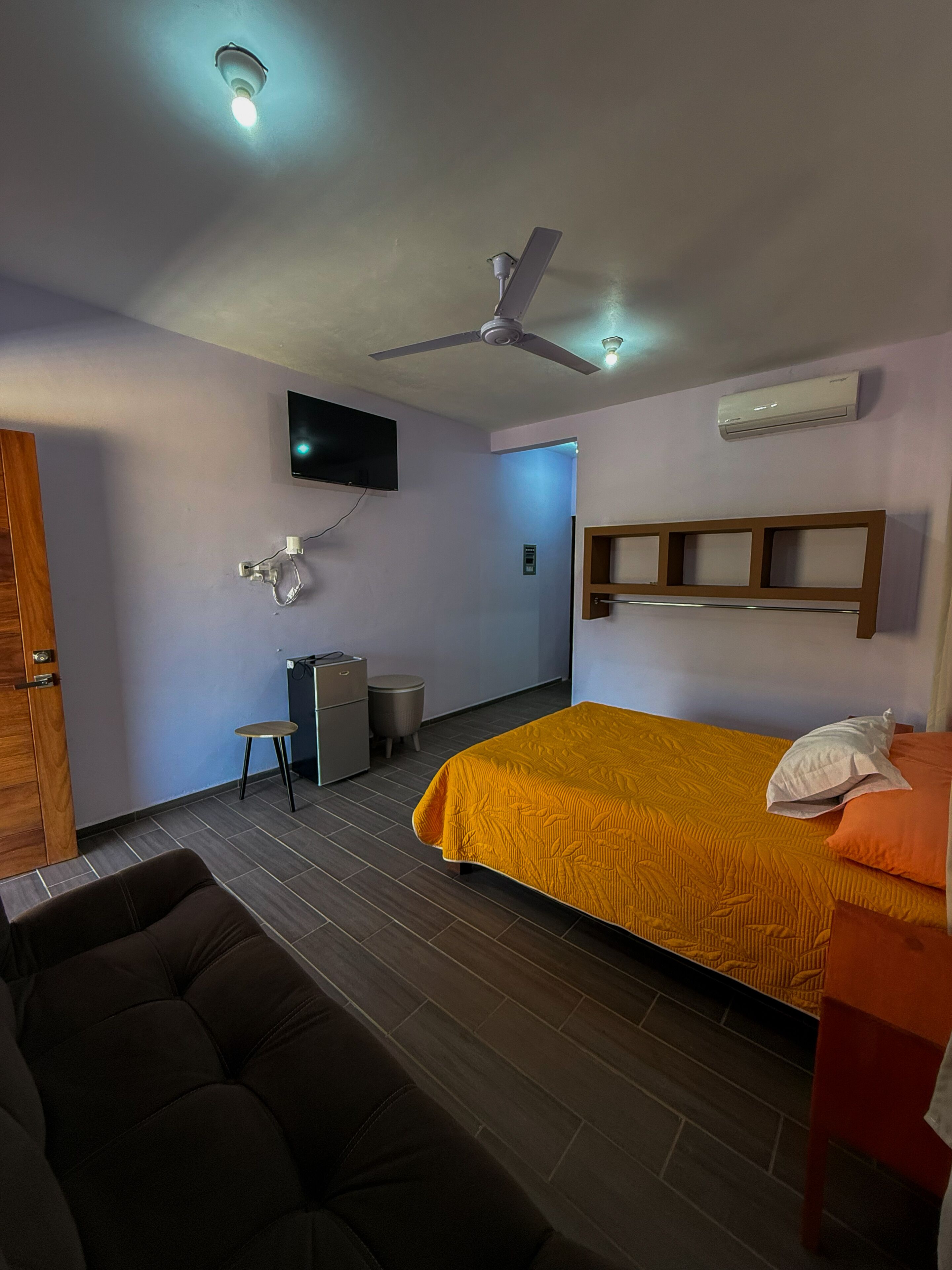 Ein Hotelzimmer mit Bett, Deckenventilator, Klimaanlage, Fernseher, Schreibtisch und Stuhl.