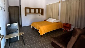 A hotel room with a bed, a chair, a small table, a ceiling fan, and a window with curtains. - Casa Mariposa (Santa Maria Huatulco)
