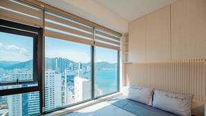 Une chambre d’hôtel avec une grande fenêtre, un lit avec une literie blanche et une vue sur la ville.