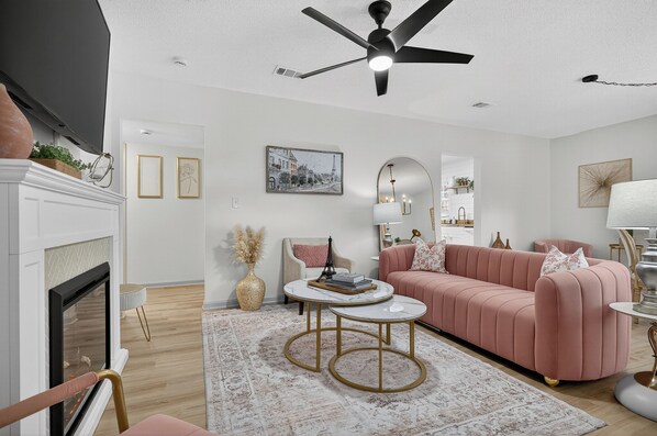 A modern living room with a fireplace, a pink sofa, a round coffee table, and a ceiling fan.