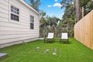 A backyard with a lawn, two white lounge chairs, and a hopscotch game.