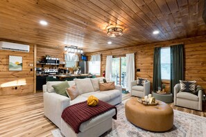A cozy cabin interior with a wooden ceiling, a sofa, a coffee table, and a kitchen area. - Whittle Escape - Sauna + Hot Tub + EV Charger (Creola)