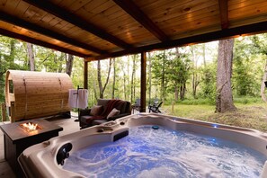 Ein Whirlpool mit Holzterrasse, Feuerstelle und Sitzbereich mit Blick auf den Wald.