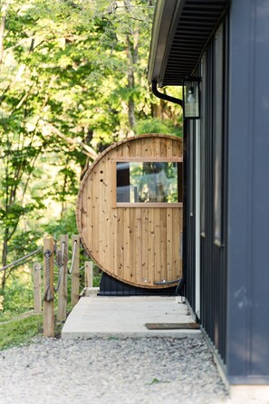 A wooden structure with a window, a wooden fence, and a gravel path leading to a building. - Whittle Escape - Sauna + Hot Tub + EV Charger (Creola)