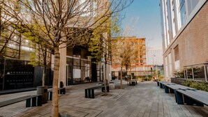Um pátio externo com bancos, árvores e edifícios modernos ao fundo.