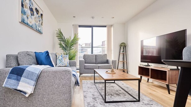 Una sala de estar moderna con un sofá gris, una mesa de centro, un televisor y una estantería.