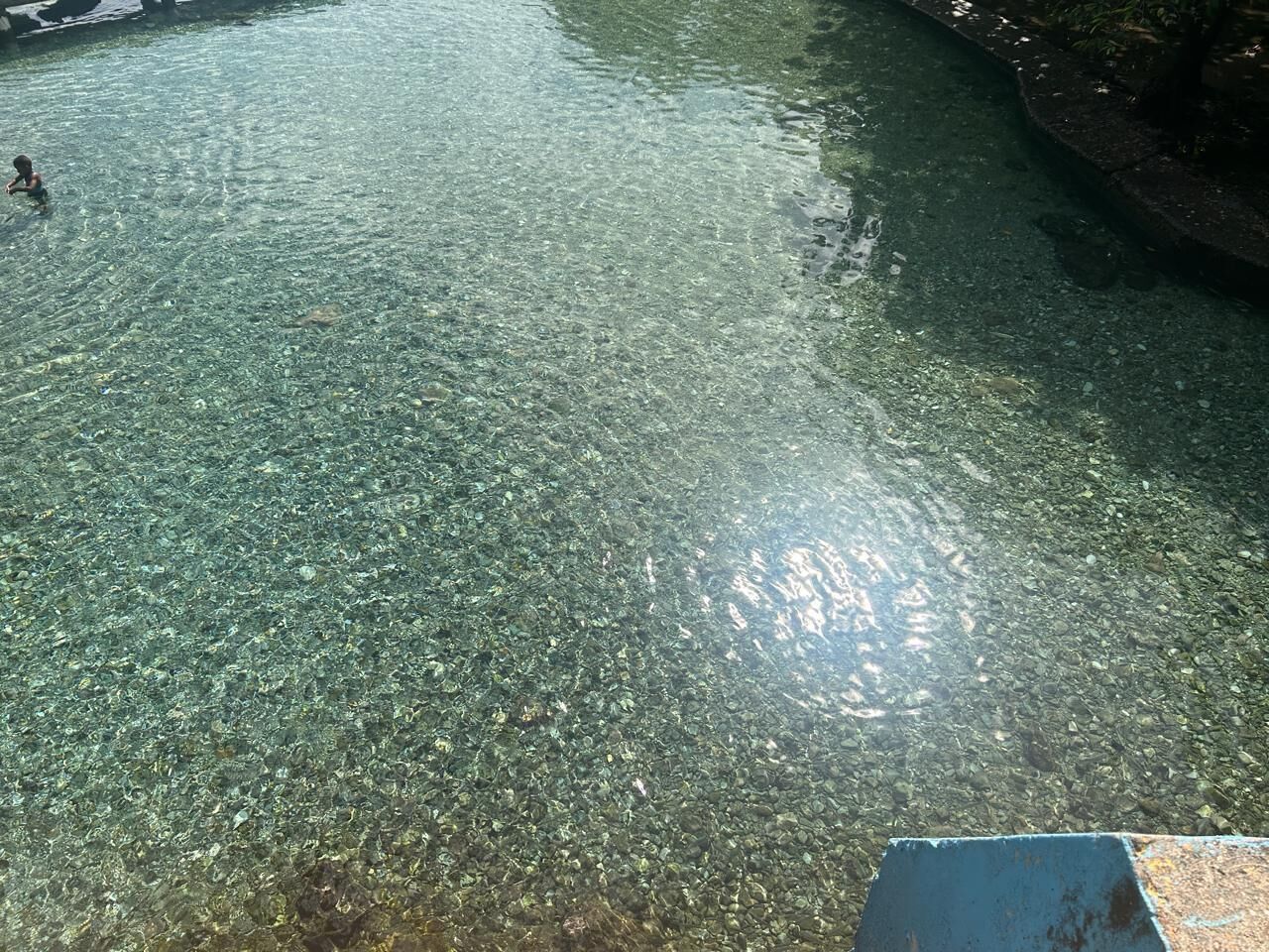 A clear pool with visible pebbles and a person in the water.