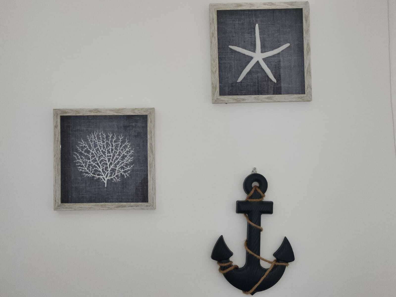 Três decorações de parede emolduradas: uma estrela-do-mar, uma árvore e uma âncora.