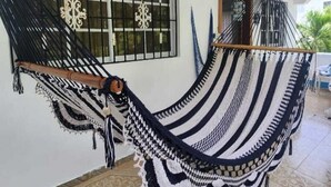 A hammock in a room with a tiled floor, a window with bars, and a door.