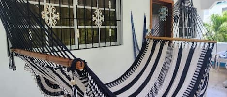 A hammock in a room with a tiled floor, a window with bars, and a door.