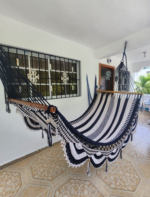 A hammock in a room with a tiled floor, a window with bars, and a door.