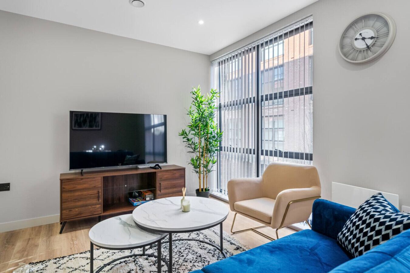 Een moderne woonkamer met een flatscreen televisie, een bank, een salontafel en een groot raam met jaloezieën.