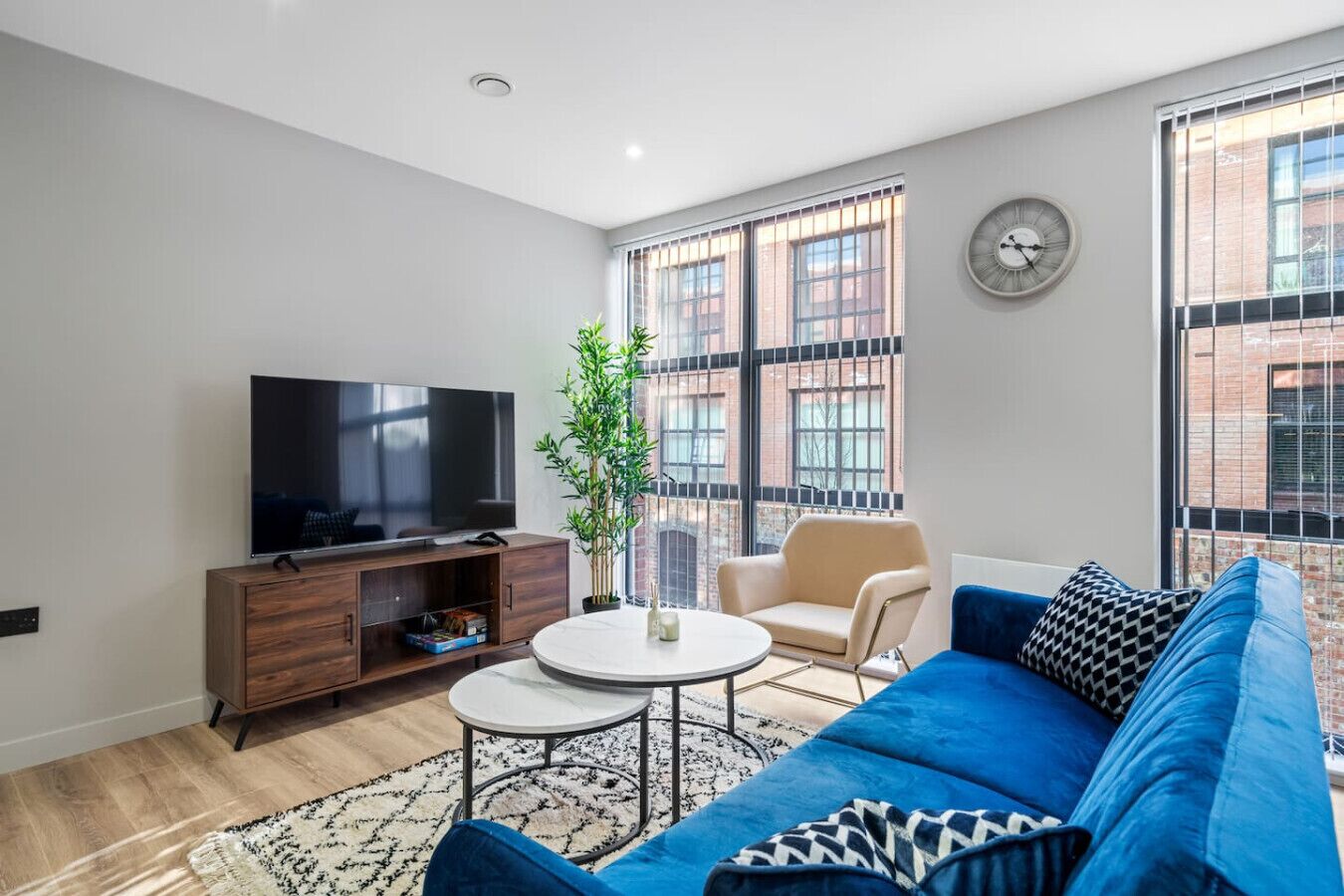 A modern living room with a flat-screen TV, a round coffee table, a blue sofa, and a potted plant.