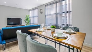 Un espace repas moderne avec une table en bois dressée pour quatre personnes, un canapé bleu et un téléviseur en arrière-plan.