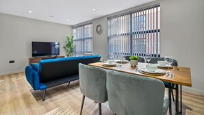 Un salon moderne avec un canapé, une table à manger pour quatre personnes et un téléviseur posé sur un meuble.