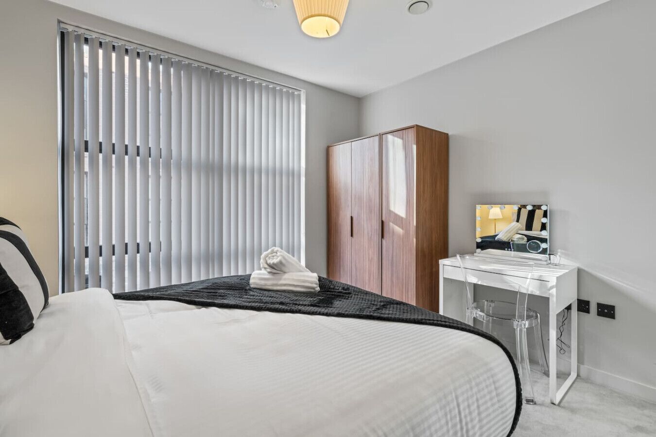 Una habitación de hotel con cama, armario, tocador con espejo y ventana con persianas.
