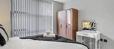 Una habitación de hotel con cama, armario, tocador con espejo y ventana con persianas.