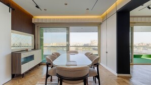 Un espace de restauration moderne, doté d’une grande table, de chaises et offrant une vue sur la ville grâce à de larges fenêtres.