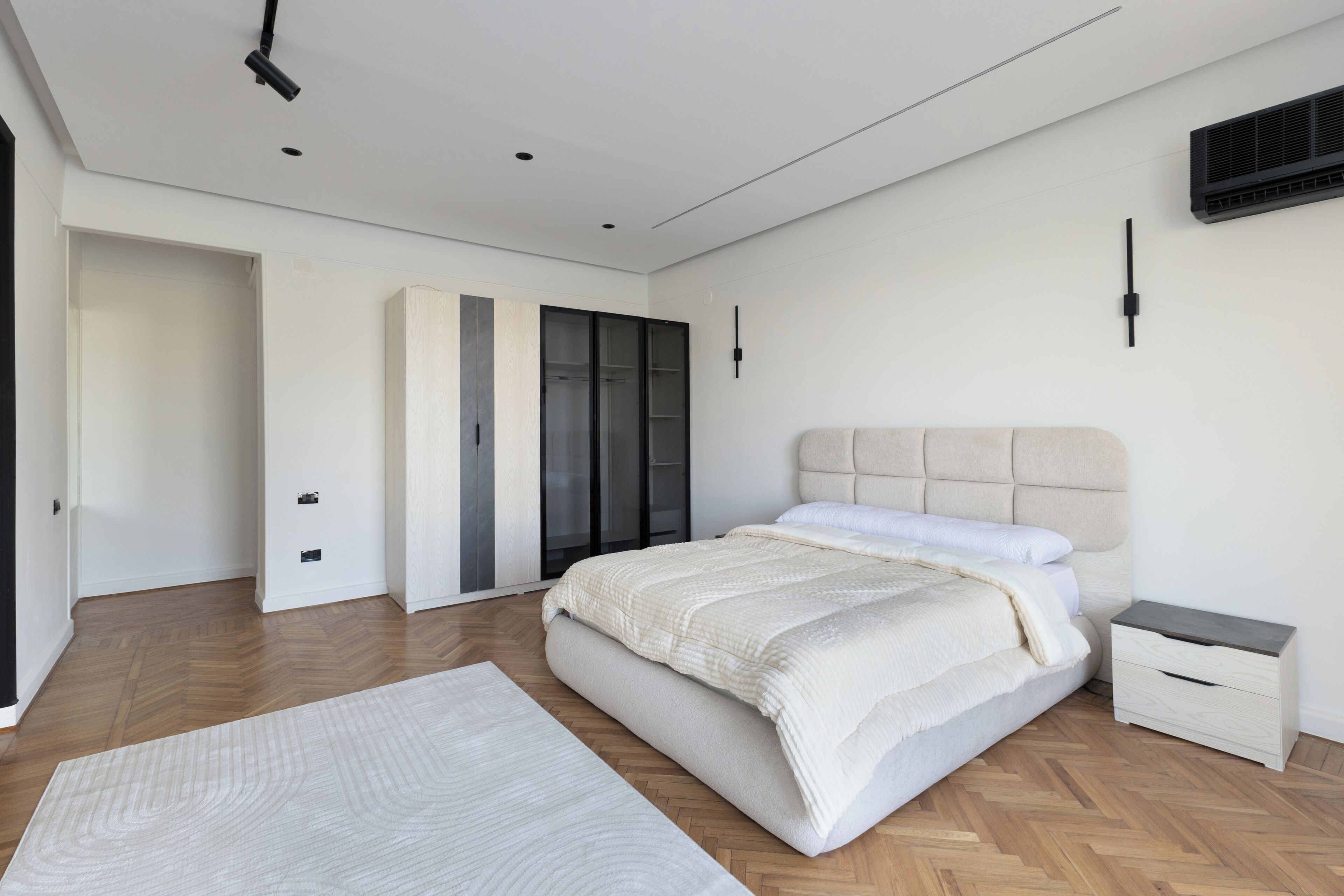 Ein modernes Schlafzimmer mit einem großen Bett, einem Nachttisch, einem Kleiderschrank und einem an der Wand befestigten Fernseher.