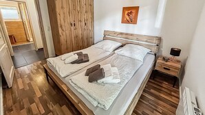 Una cama doble con dos almohadas, un armario de madera, una mesita de noche con una lámpara y un cuadro en la pared.