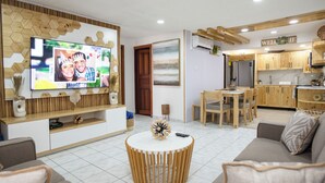 Ein modernes Wohnzimmer mit Fernseher, Holzmöbeln, einem runden Couchtisch und einer Küchenzeile mit Holzausstattung und einem Esstisch.