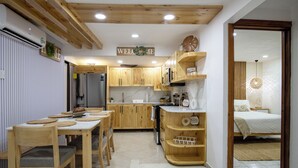 Eine kleine Küche mit Holzausstattung, ein Essbereich mit Tisch und Stühlen sowie ein Bett im angrenzenden Zimmer.