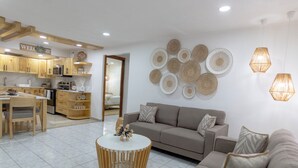 Eine moderne Küche mit Holzschränken, ein Essbereich mit Tisch und Stühlen, ein Wohnzimmer mit einer Couch und Couchtisch sowie dekorative Wandbilder.