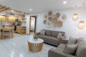 Una cocina moderna con armarios de madera, un comedor con mesa y sillas, una sala de estar con sofá y mesa de centro, y decoración mural.