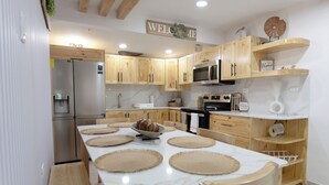 Eine moderne Küche mit Holzausbau, einem Edelstahlkühlschrank, einer Mikrowelle und einem Esstisch mit Platzsets.