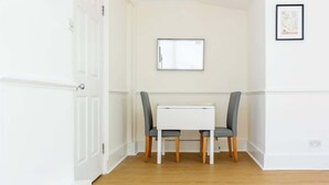 Une pièce avec une porte blanche, une table blanche et deux chaises grises, un tableau encadré au mur et un plancher en bois.
