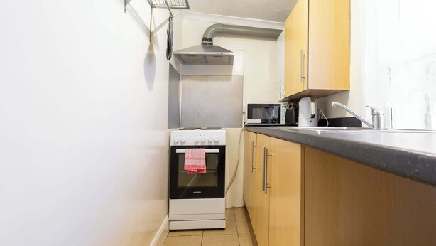 Une cuisine de taille réduite, équipée d’une cuisinière, d’un four à micro-ondes et de meubles de rangement en bois.