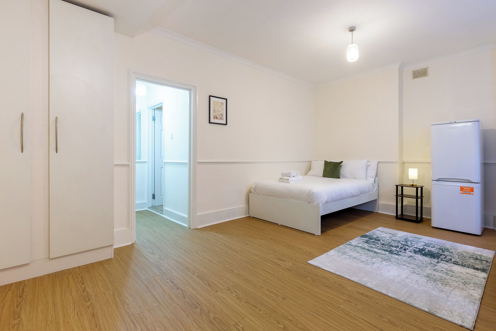 Une chambre à coucher avec un lit, une petite table de chevet, une armoire blanche et un réfrigérateur blanc.