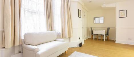 Una sala de estar moderna con un sofá blanco, una mesa de comedor con sillas y un ventanal con cortinas.