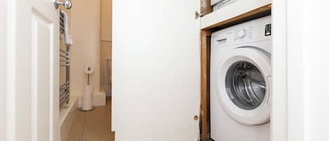 A compact laundry room with a front-loading washing machine, a toilet, and a towel rack.