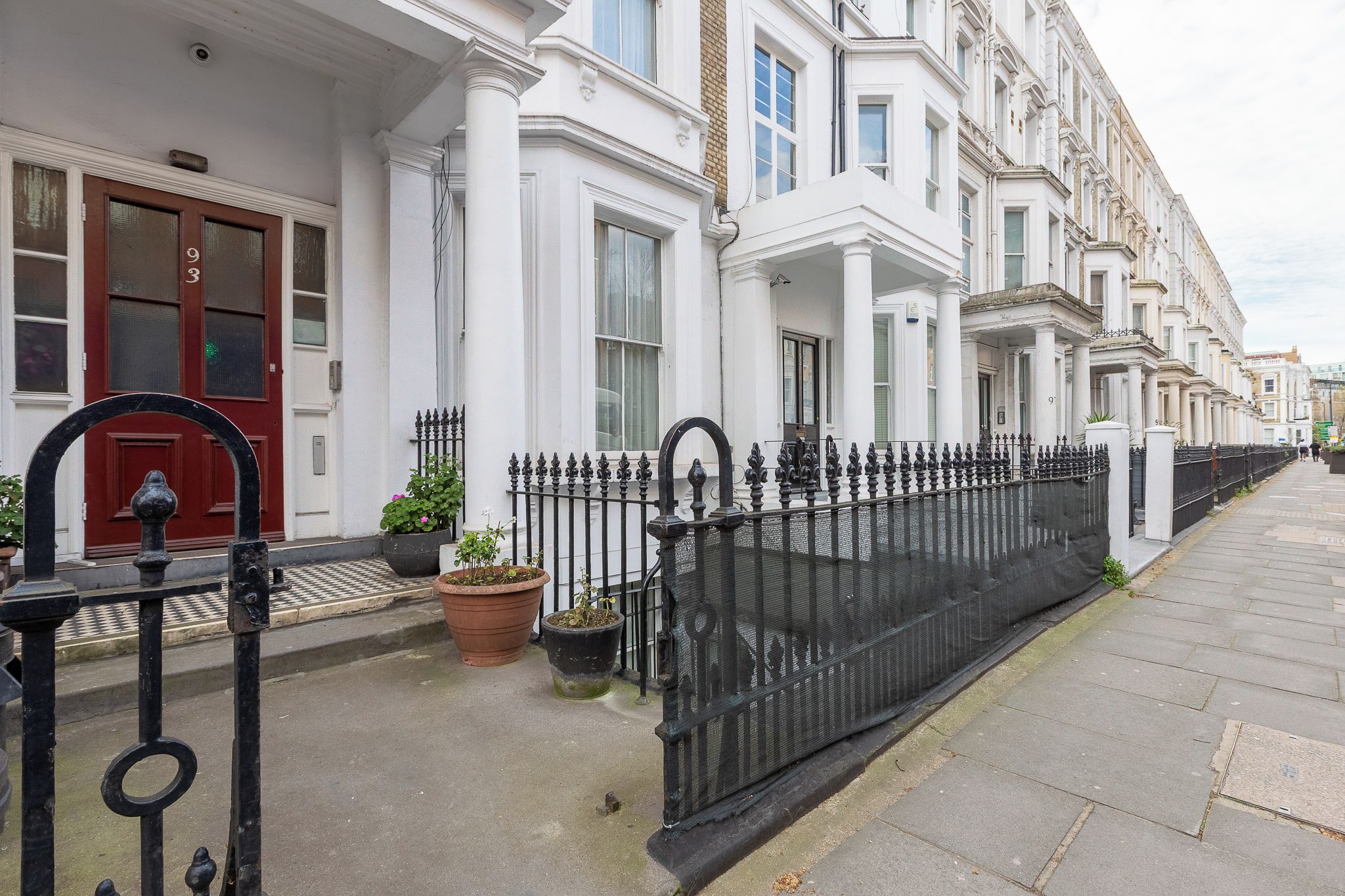 A row of white terraced houses with black iron gates and potted plants.