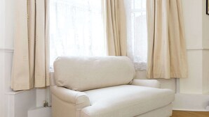 Un fauteuil blanc dans une pièce aux murs blancs, avec une fenêtre ornée de rideaux beige.
