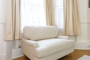 Ein weißer Sessel in einem Raum mit weißen Wänden und einem Fenster mit beigen Vorhängen.